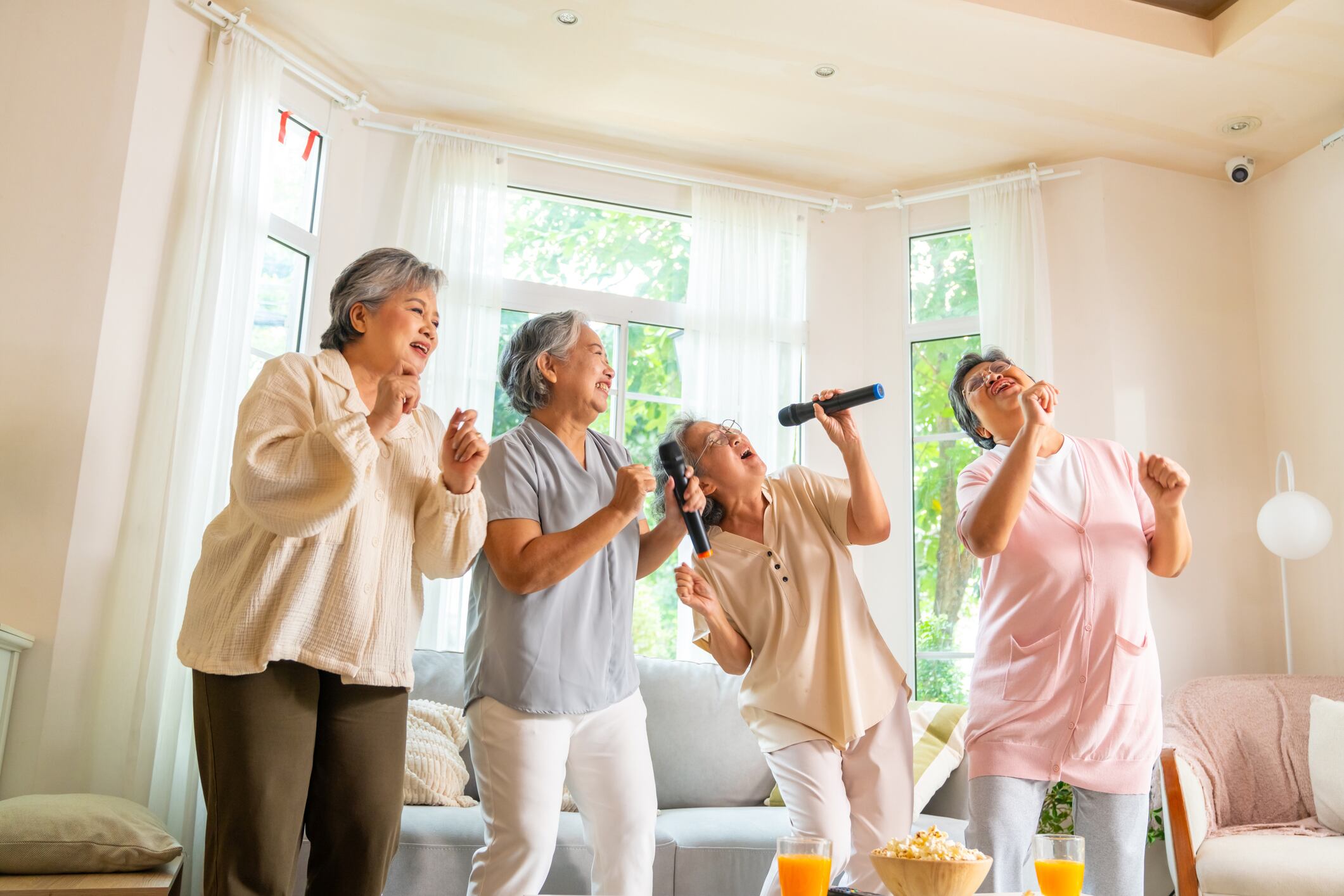 Group of Happy Asian senior women friends singing karaoke with dancing together in living room.