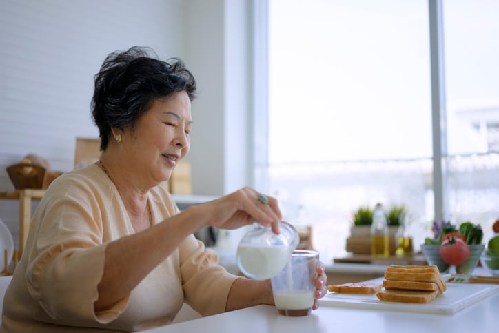An elderly woman pouring milk into a cup.