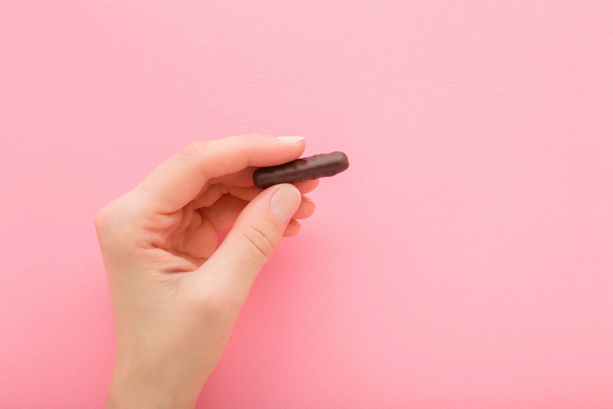 Hand fingers holding small chocolate bar. Light pink background.