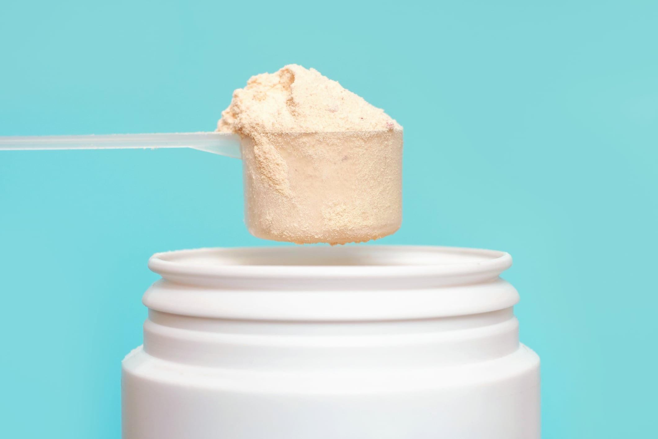 Protein powder in scoop and plastic jar on a blue background.