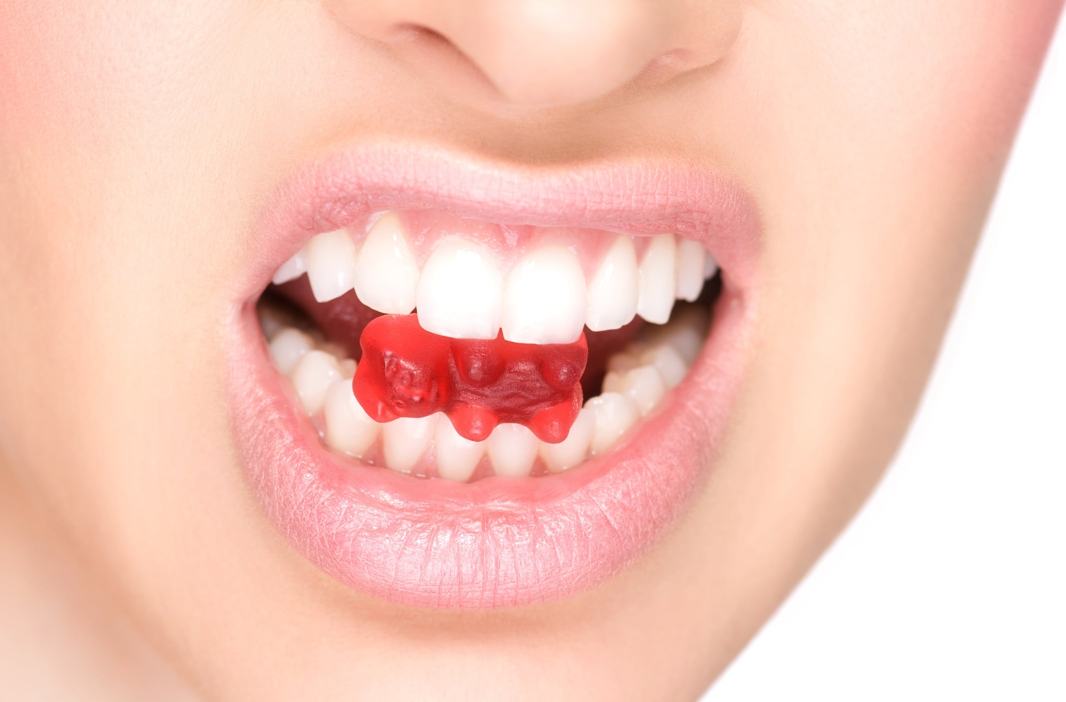 Close up of female perfectly white healthy teeth biting gummy bear candy.