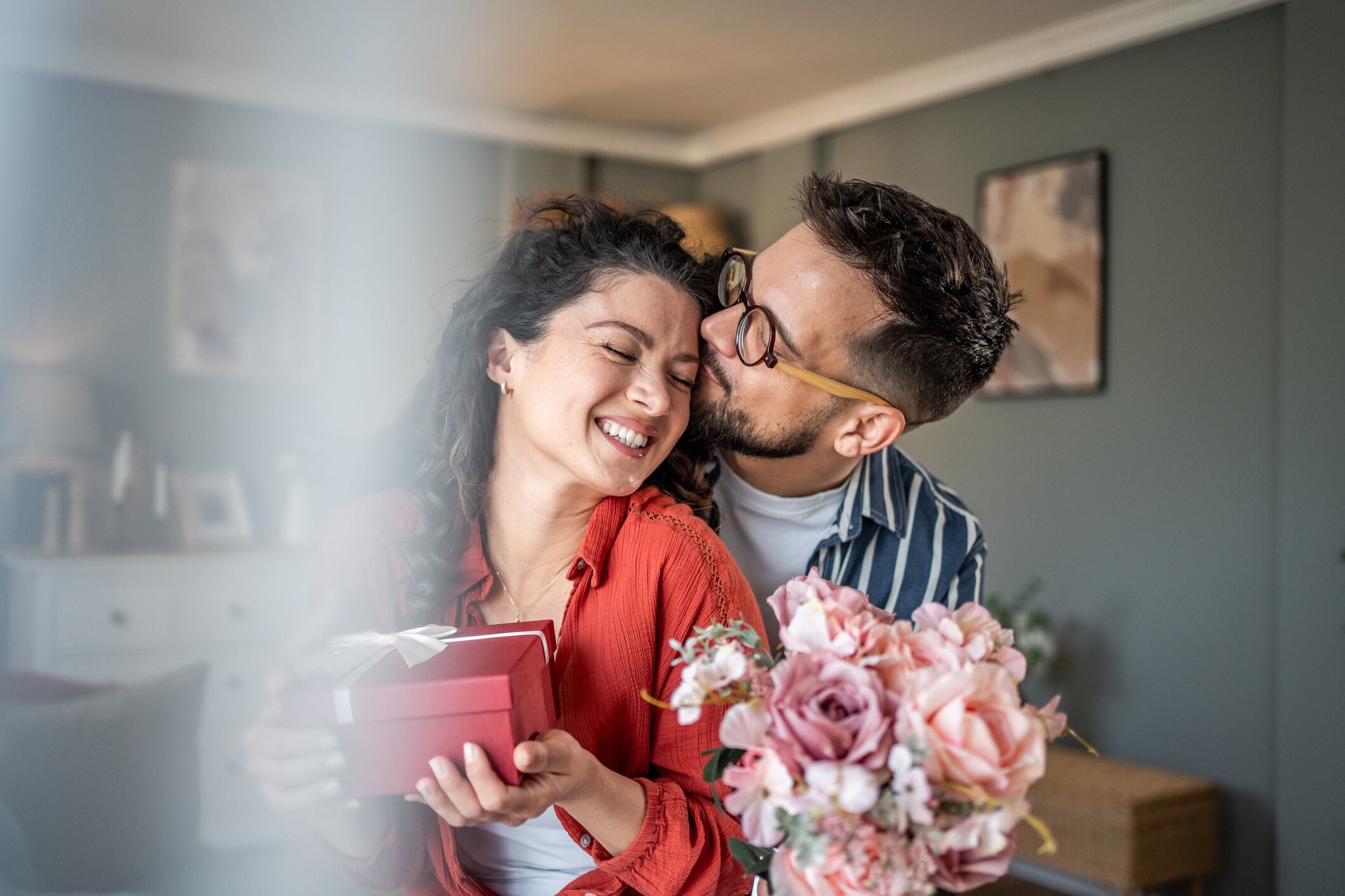 Happy couple exchanging gifts and flowers at home Milan Markovic GettyImages