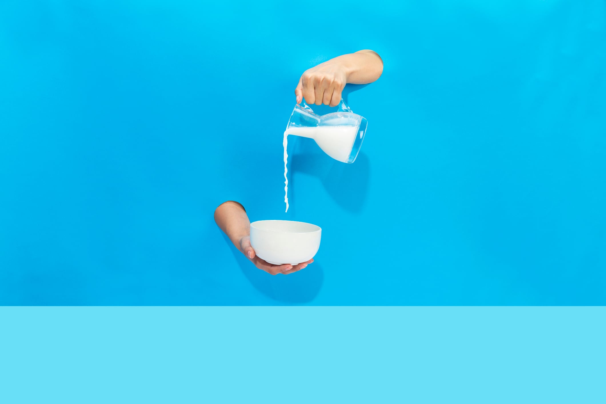 a hand pours milk from a jug into a bowl