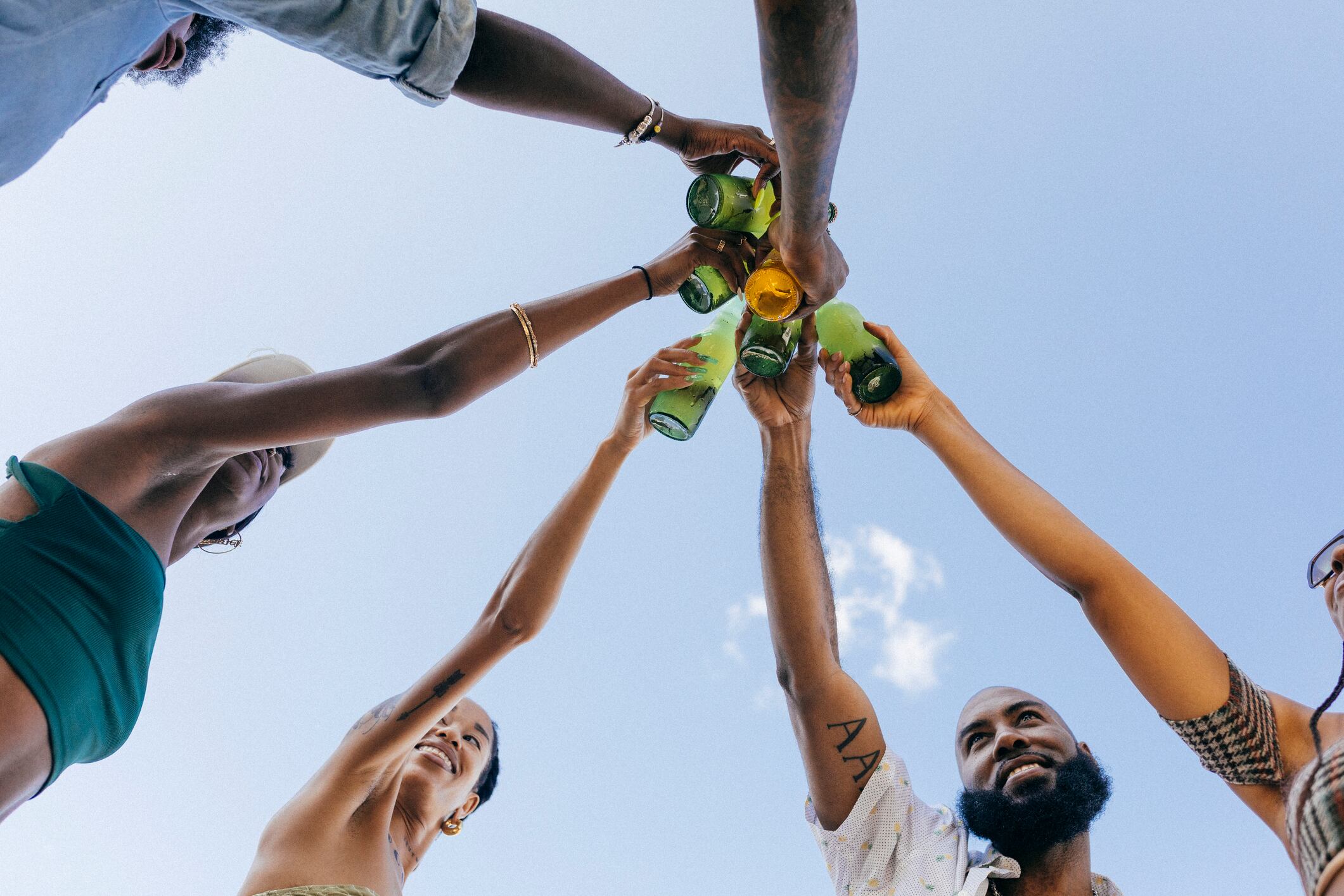 A view from underneath of friends toasting each other with beer bottles while at a rooftop party together.