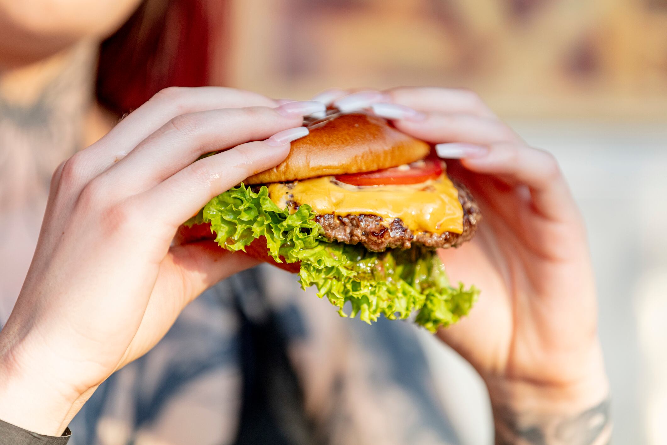 Woman holds freshly made cheeseburger outdoors in the summer sun.