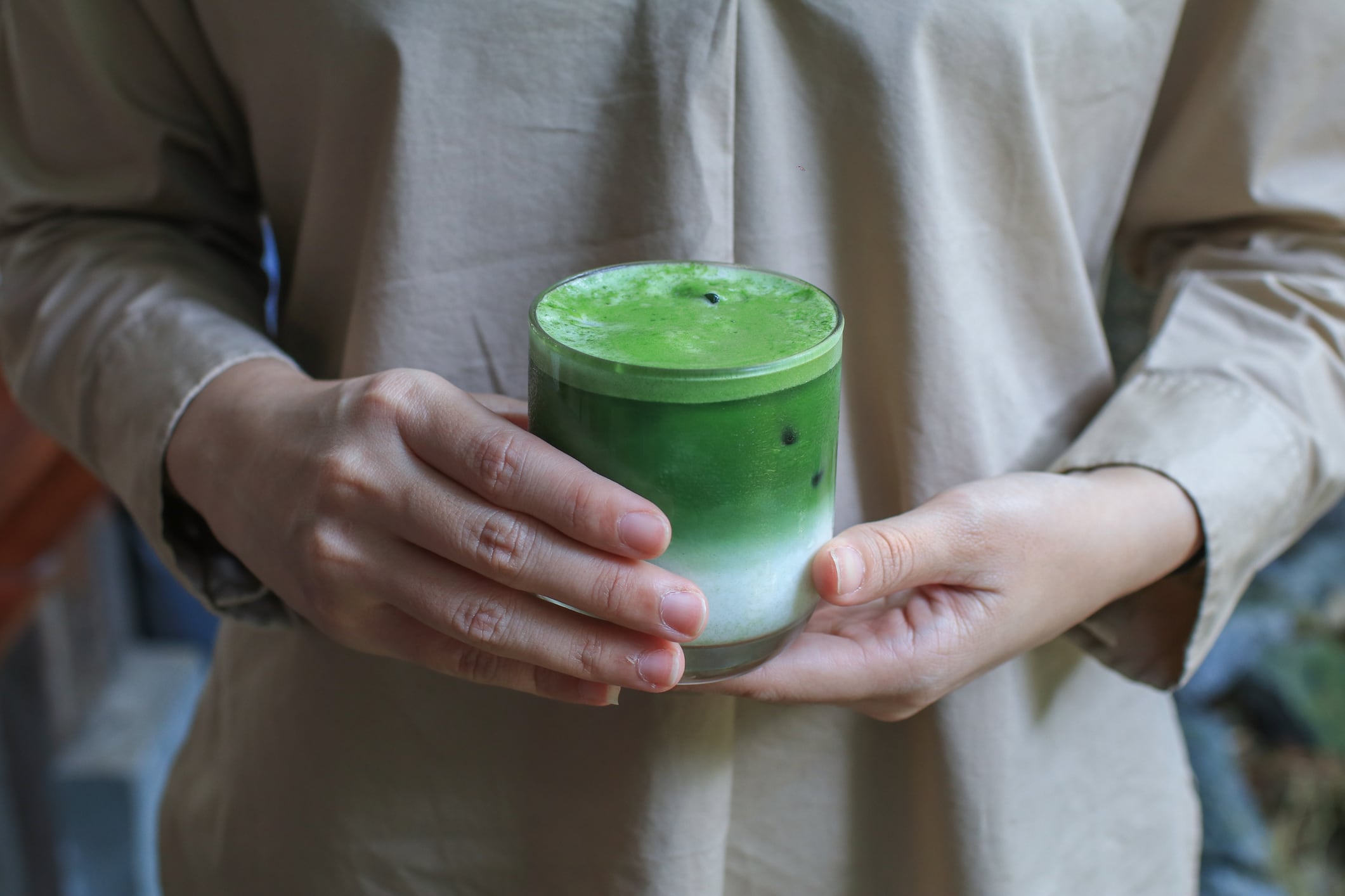 Female hand holding a glass of ice matcha green tea latte in a beautiful minimal cafe. Organic Healthy drink.