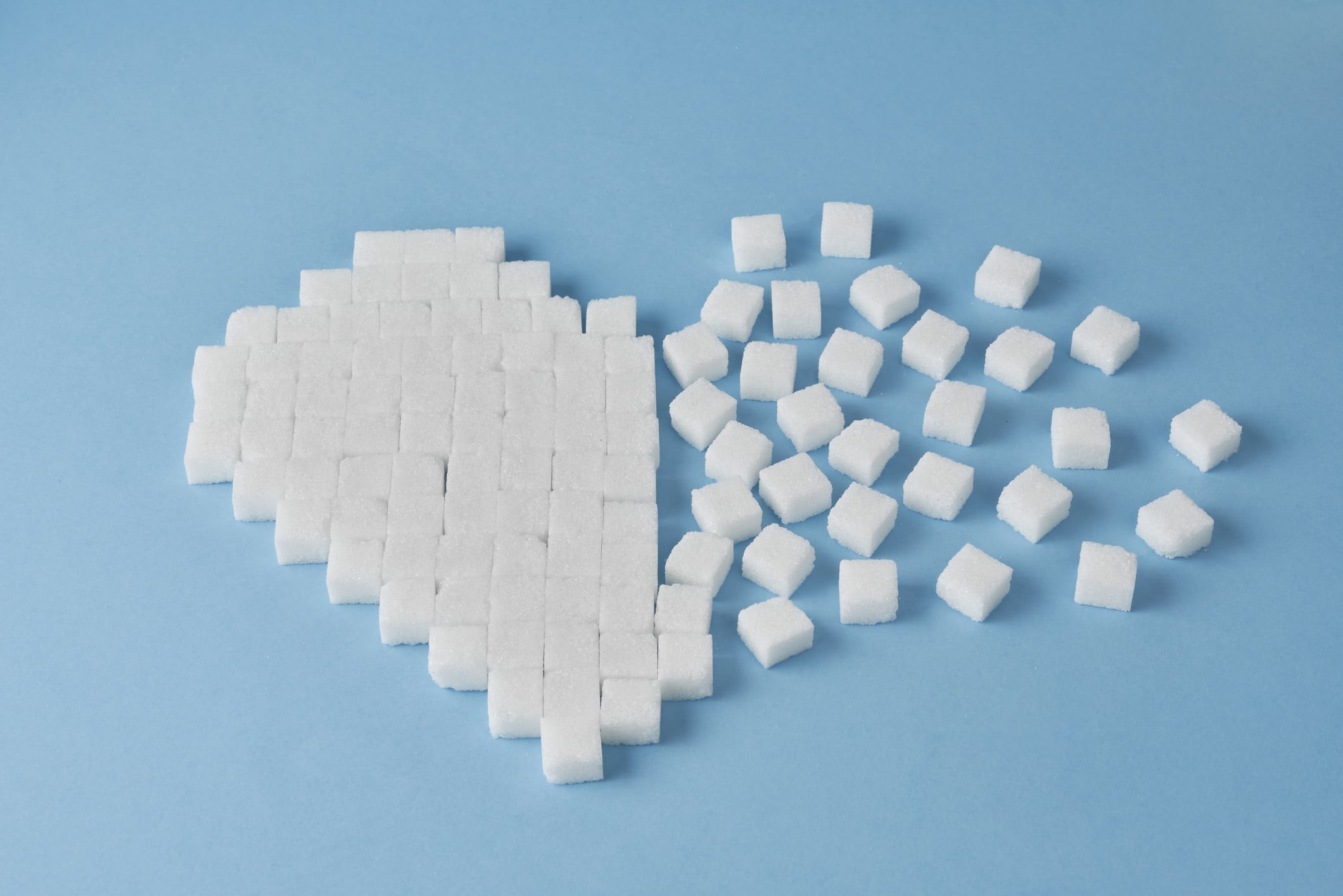 White sugar cubes arranged in a disintegrating heart on a blue background