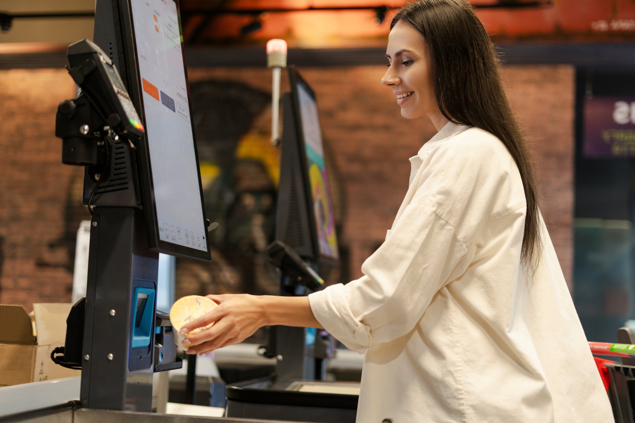Smiling Latin woman scanning groceries at a self-service checkout in a modern supermarket, enjoying the convenience and efficiency of automated shopping. Technology concept