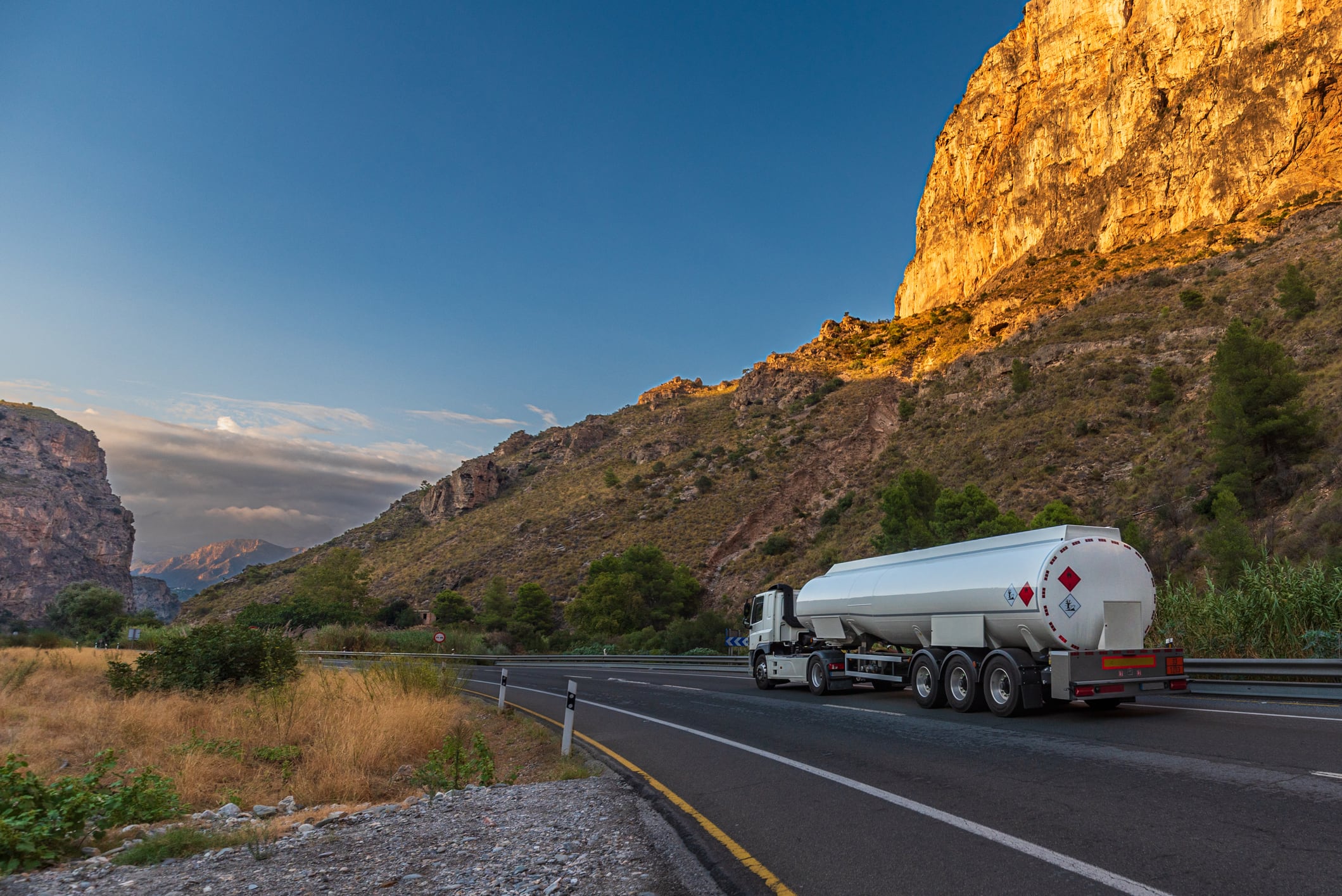 Tanker truck driving on a rural road between large mountains